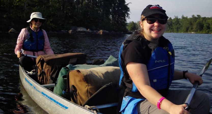 Two people wearing life jackets sit in a canoe and smile.